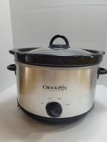 Front view of Crock-Pot slow cooker showing silver exterior, black handles and base, glass lid with black rim and handle, control knob with settings Off, Low, High, Warm.