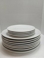 Stack of 12 white round plates, showing 6 large plates on the bottom and 6 smaller plates on top, all clean and glossy.