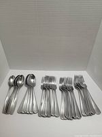 Photo showing neat rows of stainless steel cutlery including tablespoons, teaspoons, forks, and cutting utensils.