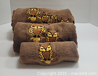 Three brown and light brown towels, rolled, featuring embroidered stylized owls in groups and singles