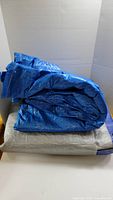 Blue outdoor tarp folded and stacked on grey tarp