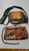 Front view of Sherpani canvas and leather crossbody bag with adjustable black strap and decorative flower design beside floral leather clutch purse with chain strap, both on white surface.