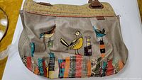 Photo of a large beige leather tote bag featuring colorful stylized birds and geometric patterns