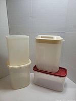 Five items including one pink insulated water bottle with strap and pouch, and four Tupperware containers in off-white translucent and clear with red lid