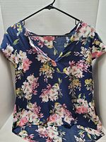 Navy floral V-neck blouse with pink and white blossoms hanging on black hanger in lightbox.