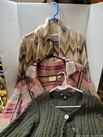 Three sweaters/cardigans hanging on separate hangers showing colors and textures