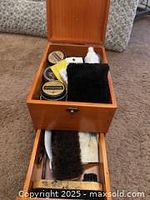 Open wooden shoe shine box showing internal storage with brushes, cloths, and polish tins visible.