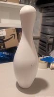 Single white bowling pin standing upright on table.