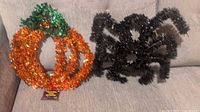 Orange and green tinsel pumpkin with black tinsel spider decoration on couch.