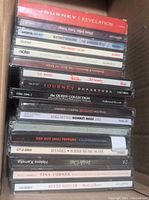 Stack of assorted CDs showing titles such as Journey - Revelation, Whitney Houston - The Greatest Hits, Phil Collins - 12" Hits and more