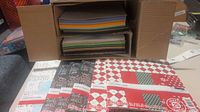 Photo showing six packs of 25 sheets of Christmas-themed cardstock in original packaging with festive patterns and colors, along with loose cardstock sheets in multiple colors stack in a box.