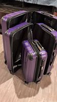 All three purple hard shell suitcases shown open with inner compartments visible, arranged from small to large size.