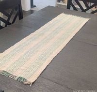 Full view of the beige and green woven table runner laid out on the table showing its length and fringe detail.