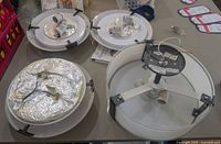 Four ceiling light fixtures laid out on table, including one large round fixture with hanging rod and three flush mount fixtures with metallic backing and wiring.