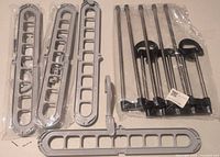 Five closet organizers laid out on a white surface, four grey plastic multi-hole hangers and one metal pants hanger with rods and clips.