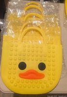 Front view of 5 yellow silicone duck popper purses stacked showing black eyes and orange duck face