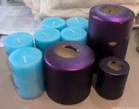 Photo showing 6 new light blue cylindrical candles and 3 used purple cylindrical candles of varying sizes with visible wear