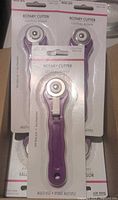 Photo showing several rotary cutters with purple handles in original packaging.