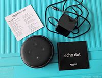 Photo showing Amazon Echo Dot device, power adapter with cable, and two booklets including quick start guide and instruction manual.