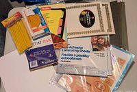 Photo showing packs of new pencils, laminating sheets, certificates, binder tabs, hanging folders, and envelopes arranged for inventory.