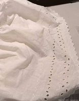 Close-up of white eyelet detail showing scalloped edges and small cut-out patterns embroidered along border.