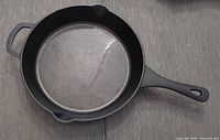 Full view of the large cast iron frying pan showing main handle and rear handle with pour spouts.