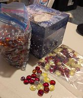 Photo of two plastic bags containing glass beads in red, yellow, and clear colors, and a decorative box with butterfly design.