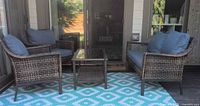 Full view of two wicker armchairs, loveseat, and glass-top table on outdoor rug