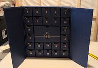 Front view of dark navy blue advent calendar box with 25 small numbered compartments inside a foldable case.
