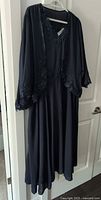 Full view of navy blue dress and matching jacket hanging on hanger, showing general style and length.