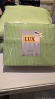 Queen sheet set and two throw pillows in vibrant lime green, packed in original packaging with label showing Textilier Pinstripe Lux and 500 thread count Egyptian cotton.