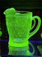 Photo under UV light showing the bright green fluorescence of the uranium glass pitcher with etched honeycomb pattern.