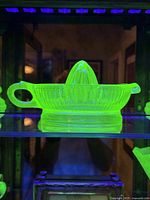 Side view of vintage uranium Vaseline glass juice reamer dish glowing bright green under UV light.