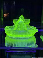 Uranium glass juice reamer glowing bright green under UV light, showing characteristic fluorescence.