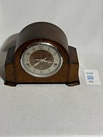Front view of vintage bentwood mantle clock with curved top and dark wood finish on a neutral surface.