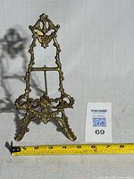 Brass easel stand shown with measuring tape for size reference, indicating width about 7 inches.