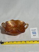 Front view of the marigold carnival glass handled dish with tape measure showing size about 7.5 inches wide.
