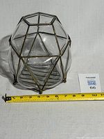 Front angle view showing the clear blown glass vase encased in geometric metal cage with a measuring tape indicating size.
