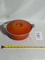Orange enamel-coated cast iron Dutch oven with lid placed on top, showing overall condition and size next to measuring tape.