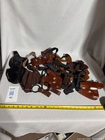 Five leather holsters and straps arranged together on white background, showing multiple holsters in black and brown leather and attached belts/straps.