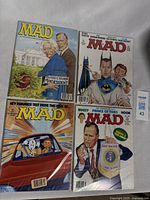 Four vintage Mad Magazine comic books in plastic sleeves laid out flat on a soft surface, showing distinct cover art.