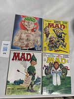 Four vintage Mad Magazine comic books laid out showing colorful and artistic covers with caricatures and satire themes.