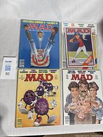 Four vintage Mad Magazine comic books displayed on flat surface, colorful illustrated covers visible.