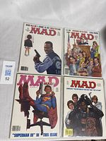 Four Mad Magazine comic books laid flat showing front covers with colorful humorous artwork and identifiable issue details
