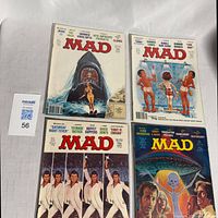 Four vintage Mad Magazine comic books laid out, showing various cover art including Jaws parody and disco themes