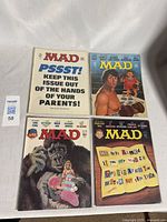 Photo showing all four Mad Magazine comic books laid out flat with full cover view.