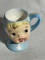 Front angle showing detailed child's face with blonde hair and facial features on ceramic egg cup.