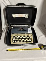 Vintage SCM Smith Corona Galaxie Deluxe typewriter inside its original hard carrying case, accompanied by a measuring tape for scale.