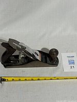 Side angle showing the full length of the Stanley No. 4 wood hand plane with wooden knob and handle next to a measuring tape showing approx 9 inches length.