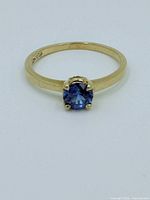 Front view of 10K gold ring with round blue topaz gemstone set in four prongs.